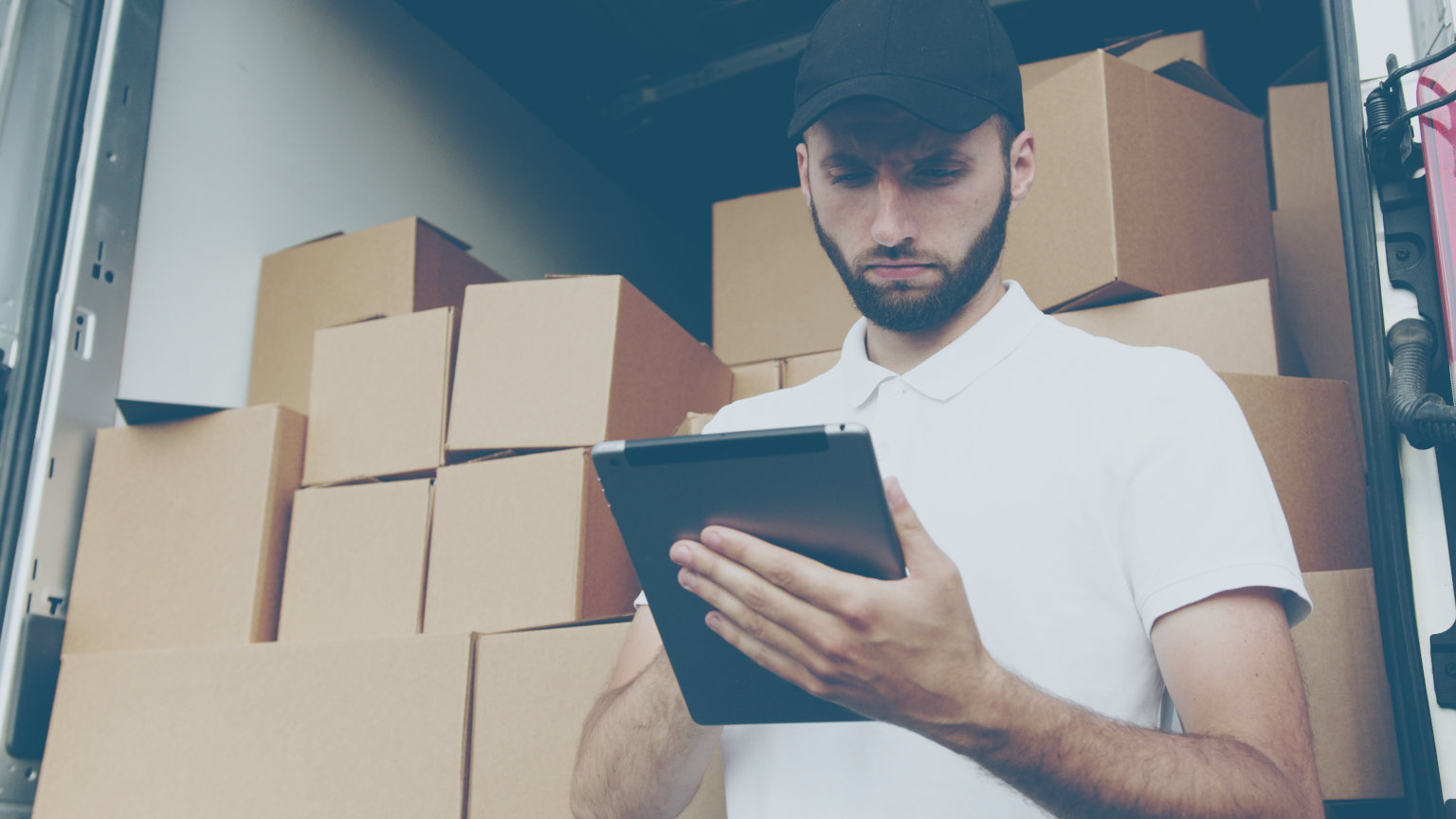 Guy standing in front of a moving truck full of boxes looking at a tablet